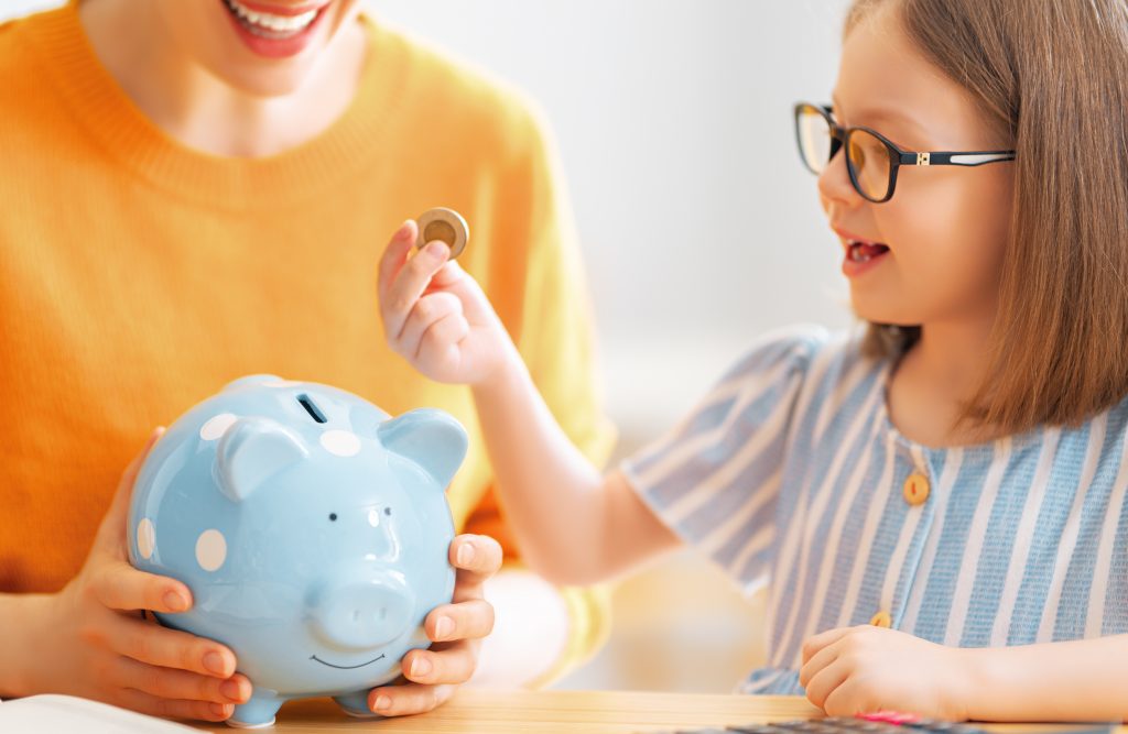 Woman,And,Child,Sitting,At,Desk,With,A,Piggy,Bank